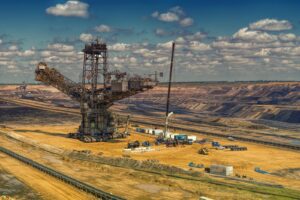 Aerial view of heavy machinery operating in a vast open-pit mine under a cloudy sky.